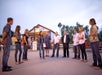 A group of eleven adults stand in a loose circle outside a rustic building at dusk, engaged in conversation.