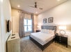 A modern bedroom with a large bed, two bedside tables with lamps, a ceiling fan, a window with curtains, a TV on the wall, and neutral-colored decor.