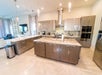 Modern kitchen with beige cabinets, marble countertops, stainless steel appliances, and pendant lights, adjacent to an open living area.