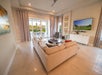Modern living room with a beige sectional sofa, large TV, glass doors opening to a patio, and neutral decor.