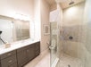 Modern bathroom with a double-sink vanity, large mirror, glass-enclosed shower, and a toilet partially visible behind the shower wall.