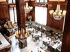 View looking down on a dining room with dark wooden walls, large windows, several chandeliers, and several tables and booths.