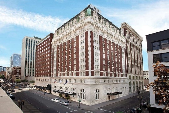 Exterior view of the corner of The Benson Portland, a large white and red brick building with several stories, and a blue cloudy sky overhead.