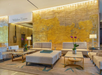 Hotel lobby with beige sofas, coffee tables, and purple orchids. A gold textured wall serves as a backdrop with "Wilshire Tower" signage above. Warm lighting creates a cozy atmosphere.