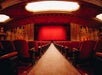 Ornate theater interior with red velvet seats and a red curtain on stage, viewed from the aisle center.