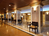 Spacious hotel lobby with polished floors, ornate columns, wall sconces, and wooden chairs lining the walls.