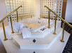 Jacuzzi tub surrounded by glass block walls and gold handrails, with neatly stacked towels and toiletries on a white platform.