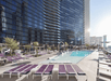 Modern outdoor hotel pool area with purple loungers, a small pool, and high-rise buildings in the background on a sunny day.