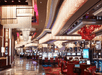 Elegant casino interior with rows of gaming machines, ornate chandeliers, and red seating. Bright lighting highlights the reflective flooring and lavish décor elements.