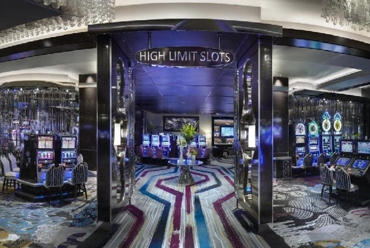 Entrance to a casino high limit slots area with neon lights, slot machines, and colorful carpet.