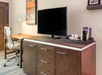 Hotel room with a TV on a wooden dresser, a coffee maker and cups on a tray, and a desk with a chair and a lamp in the background.