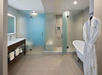 Modern bathroom with a vanity, towel rack, freestanding bathtub, and separate shower area. Walls and floors are tiled in neutral colors, and a robe hangs on a hook.