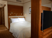 A hotel room with a white king bed with lamps over it and a partition in front of it with a TV on the other side.