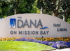 Sign reading "The Dana on Mission Bay Hotel & Marina" with flowers and grass in the foreground.