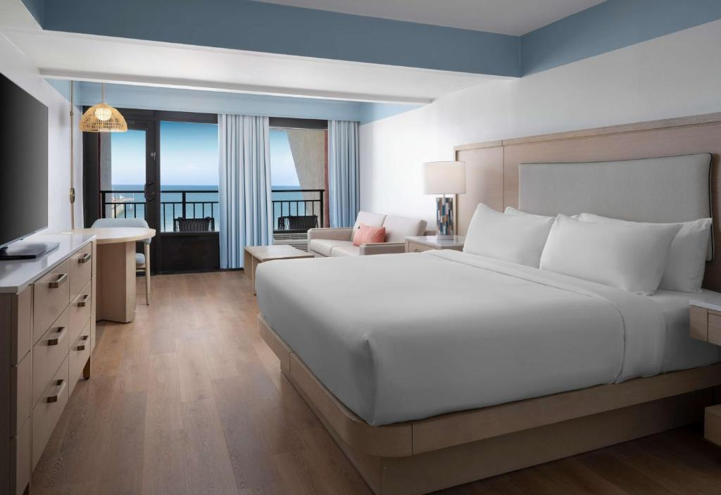 Guest room with one king bed, sofa bed, flat-screen TV, and balcony with ocean view.