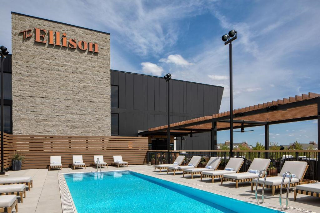 Rooftop pool with lounge chairs, a pergola, and the word "Ellison" on a modern building. Clear blue sky in the background.