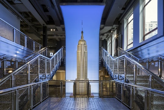 Exhibit of the Empire State Building inside a modern interior, flanked by symmetrical staircases with metal railings under a blue-lit archway.