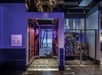 A dimly lit, vintage elevator with a metal accordion gate and ornate interior. Controls and machinery are visible on the right. Purple and black color scheme.