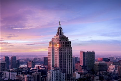 The Empire State Building at sunset with a colorful sky, surrounded by other skyscrapers in New York City.
