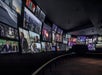 A dark room with numerous screens displaying various images, including people and cityscapes, covering the walls.