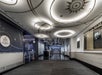 Modern hallway with decorative ceiling lights and patterned walls. Signs indicate WiFi availability and a cinema entrance. A patterned carpet covers the floor.