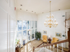 Bright foyer with a large chandelier, two yellow armchairs, a small table, and framed artwork. A staircase leads down to glass doors with plants nearby.