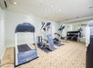 Small gym room with a treadmill, stationary bike, elliptical machine, and a rack of dumbbells. A full-length mirror covers one wall.