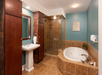Modern bathroom with teal walls, brown tile flooring, glass-enclosed shower, large corner bathtub, pedestal sink, and wooden cabinets.