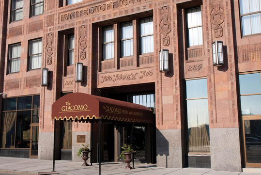 Entrance of The Giacomo hotel with a brown canopy, large windows, and detailed brickwork on the building facade.