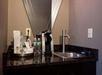 A kitchenette area with a sink, a coffee maker, water bottles, cups, an ice bucket, a menu, and a mirror on the wall behind the counter.