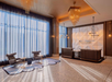 Modern hotel lobby with geometric wall design, reception desk, two armchairs, round side tables, large windows with sheer curtains, and chandeliers.
