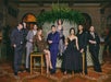 A group of seven people in formal attire pose in front of a large indoor planter in an elegant setting.