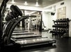 Row of treadmills in a gym with weight racks and various exercise equipment in the background.