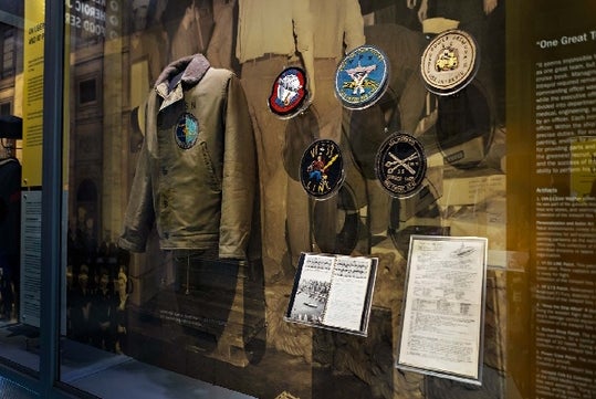 A display of old military uniforms and several different styles of patches with on hand written documents at the bottom of the display.