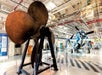 A rusted propeller on display on the hanger deck at the The Intrepid Sea, Air & Space Museum with a large plane in the background.