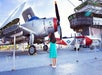 A little girl in a bright blue dress standing at a guard rope looking at the older gray plane on the other side of it at The Intrepid Sea, Air & Space Museum.