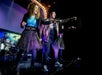 Performers in colorful outfits sing and point on a stage with a drummer in the background.