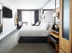 Guest room with a king bed, work desk, and chair, armchair and large windows with black out drapes.