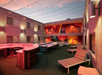 Outdoor courtyard with string lights, bar, barstools, and lounge chairs. Artwork decorates the walls. Twilight setting with a warm, inviting atmosphere.