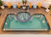 Aerial view of a swimming pool with a connected circular hot tub, surrounded by yellow chairs and striped footstools on a beige pool deck.