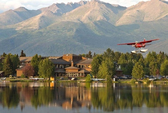 View of Lakefront Anchorage on the shore of Lake Spenard, a sea plane, and the majestic Chugach Mountains behind.