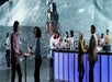 People socializing in a futuristic space-themed bar, with a lunar landscape and lunar module projected in the background.