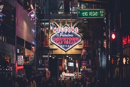 Crowd walking under illuminated "Welcome to Fabulous Downtown Las Vegas Nevada" sign at night, surrounded by neon lights and street signs.