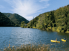 Wide shot of two people in yellow kayak in the dark water of the Blue Lakes with lush forrest on the land around them on a sunny day.