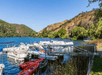 A small marina full of boats and kayaks in the dark blue water of the Blue Lakes with the mountains in the background on a sunny day.
