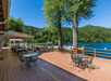 A partially covered wooden deck with several sets of iron patio furniture on it and a deep blue lake with boars in it in the background.