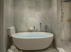 A modern bathroom with a large oval bathtub, wall-mounted shower, and minimalist decor. Rolled towels and bath products are neatly arranged.