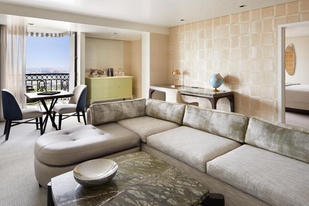 A modern living room with a sectional sofa, a coffee table, a dining area with two chairs, a desk with a globe, and a window with a view.