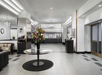 Spacious hotel lobby with a round glass table holding a flower arrangement, tiled floors, chandeliers, reception desks, and black-and-white framed wall art.