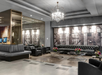 Modern hotel lobby with black leather sofas, glass coffee tables with flower arrangements, large wall art, mirrored accents, and a chandelier.